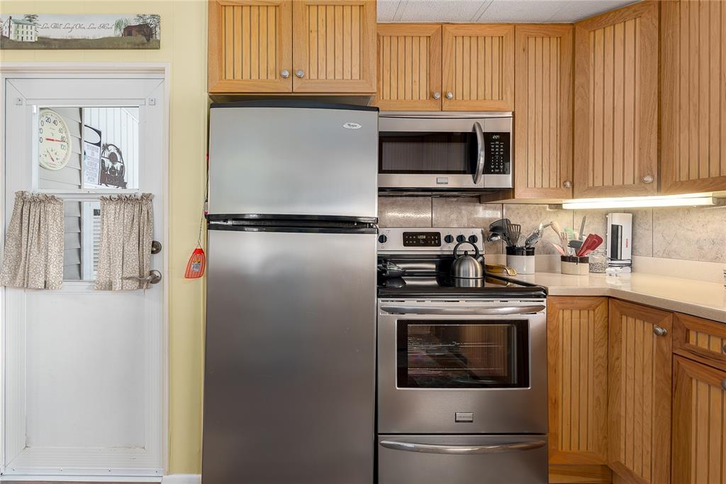 A kitchen features stainless steel appliances, light wood cabinetry, and a door with curtains — 198 TANKEY DRIVE, PALMETTO, FL