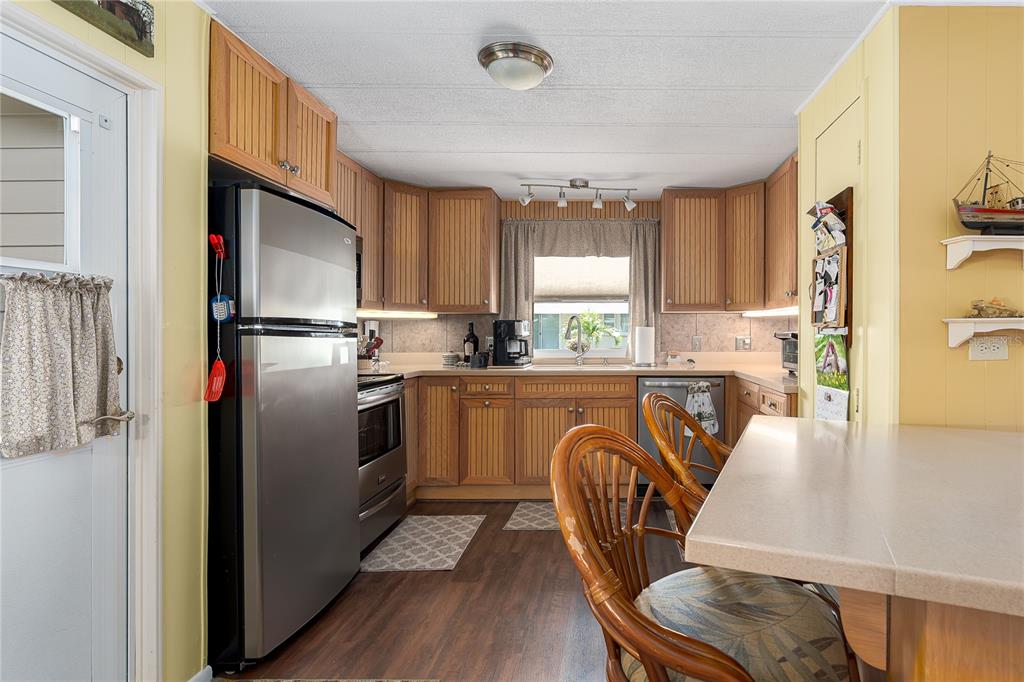 A kitchen features wood-paneled cabinets, stainless steel appliances, and a breakfast bar with rattan chairs — 198 TANKEY DRIVE, PALMETTO, FL