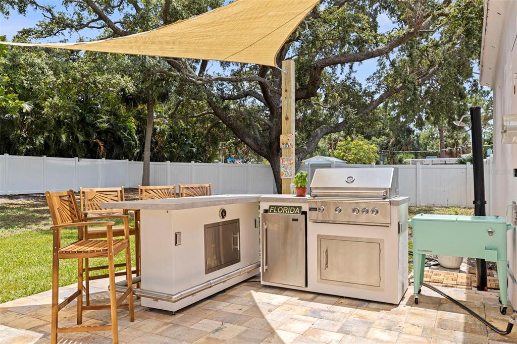 An outdoor kitchen with a grill, stainless steel cabinets, and bar seating on a patio — 1579 BAYSHORE BOULEVARD, DUNEDIN, FL
