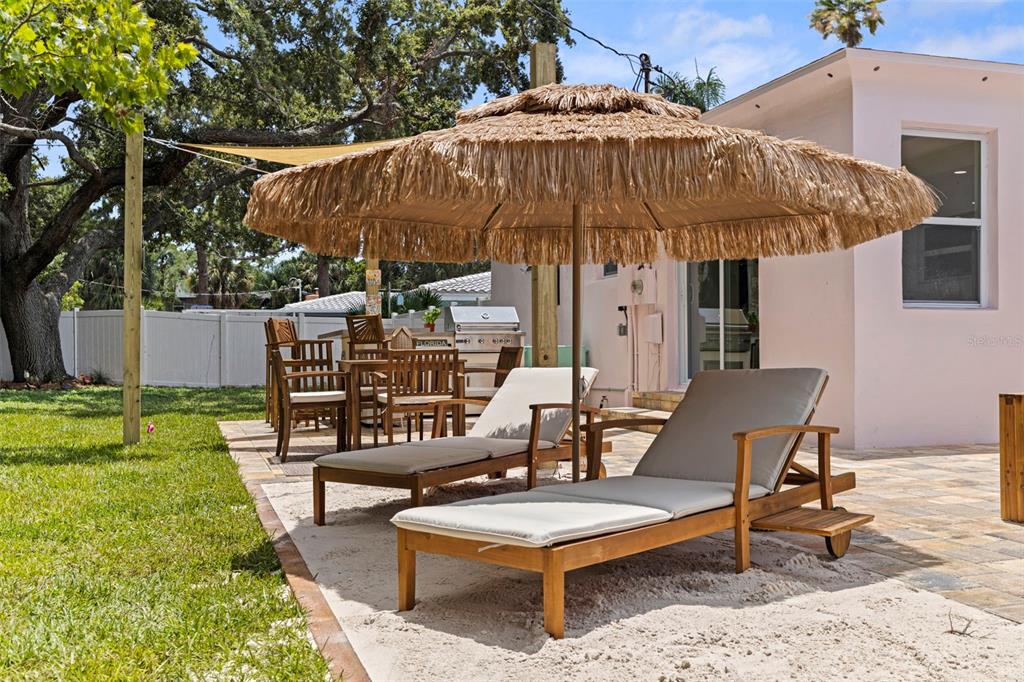 A backyard patio features a thatched umbrella, two lounge chairs, and a dining set — 1579 BAYSHORE BOULEVARD, DUNEDIN, FL