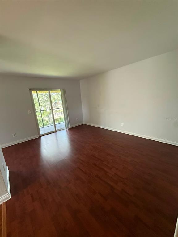 An empty room with dark wood-look flooring, light gray walls, and a sliding glass door — 2400 BARLEY CLUB COURT UNIT 3, ORLANDO, FL