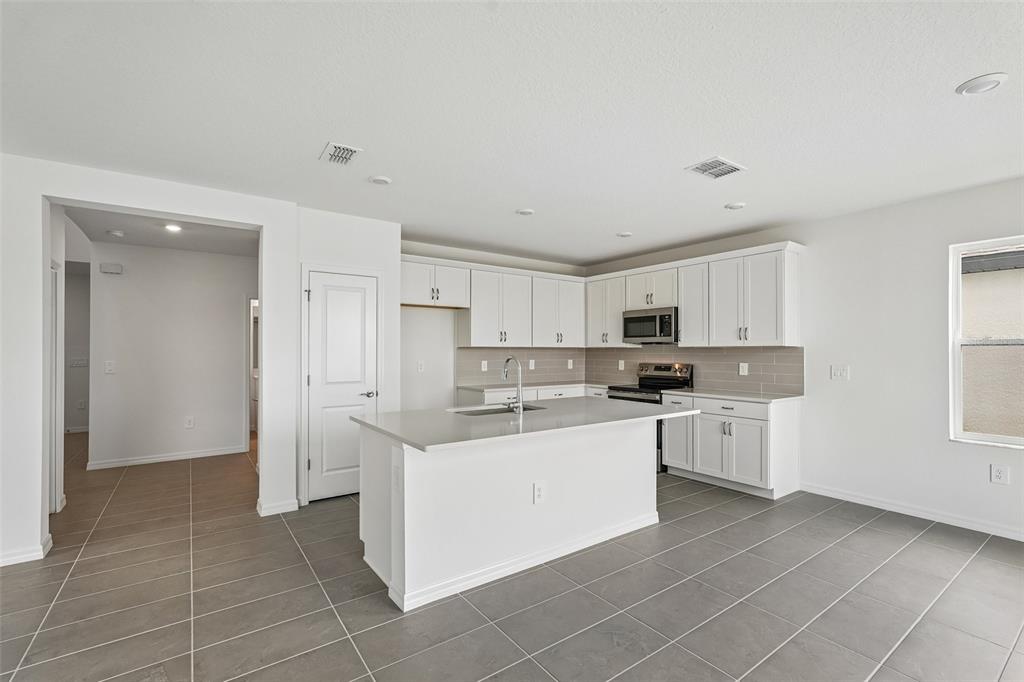 A modern kitchen features white cabinets, a central island, and gray tile flooring — 4327 OUTHAUL RUN, PALMETTO, FL