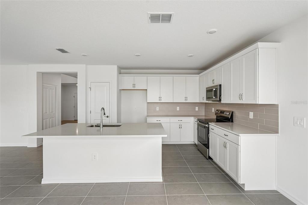 A modern kitchen features white cabinets, stainless steel appliances, a center island, and tile flooring — 4327 OUTHAUL RUN, PALMETTO, FL