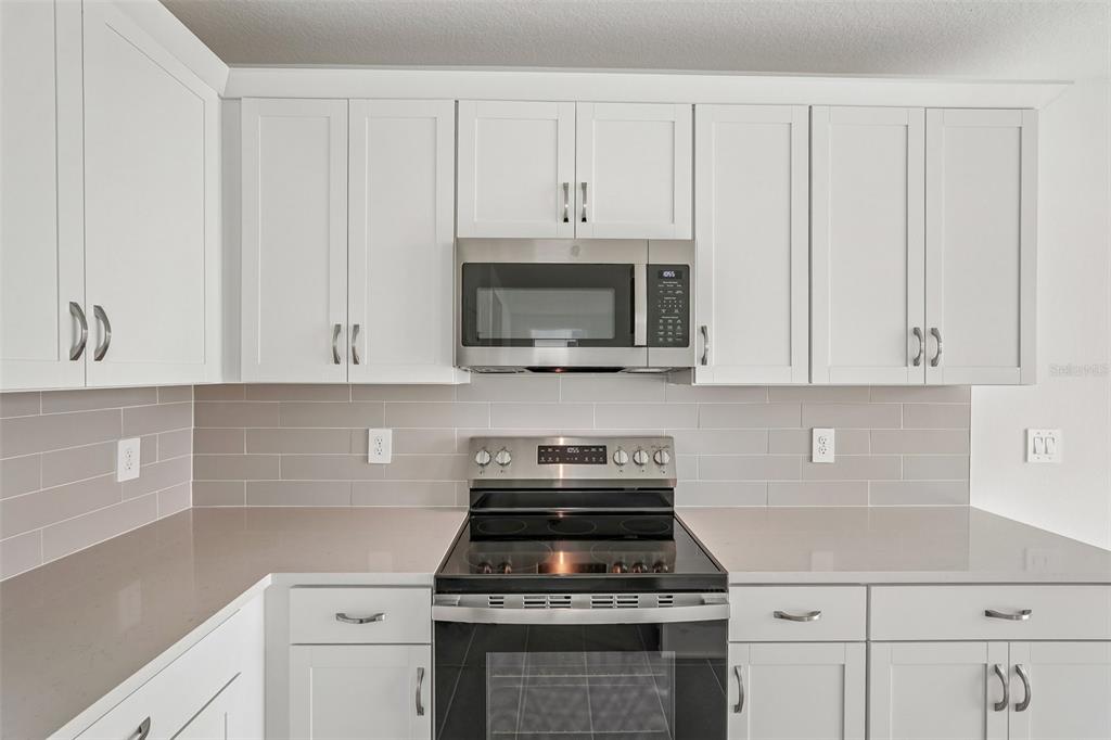 A kitchen features white shaker cabinets, a stainless steel microwave, a range, and gray backsplash — 4327 OUTHAUL RUN, PALMETTO, FL