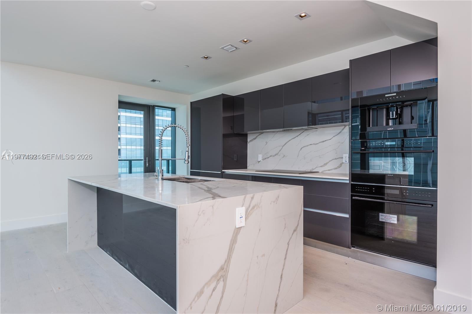 A modern kitchen features dark cabinetry, a marble waterfall island, and stainless steel appliances — 1451 Brickell Ave # 4004, Miami FL 33131, MIAMI, FL