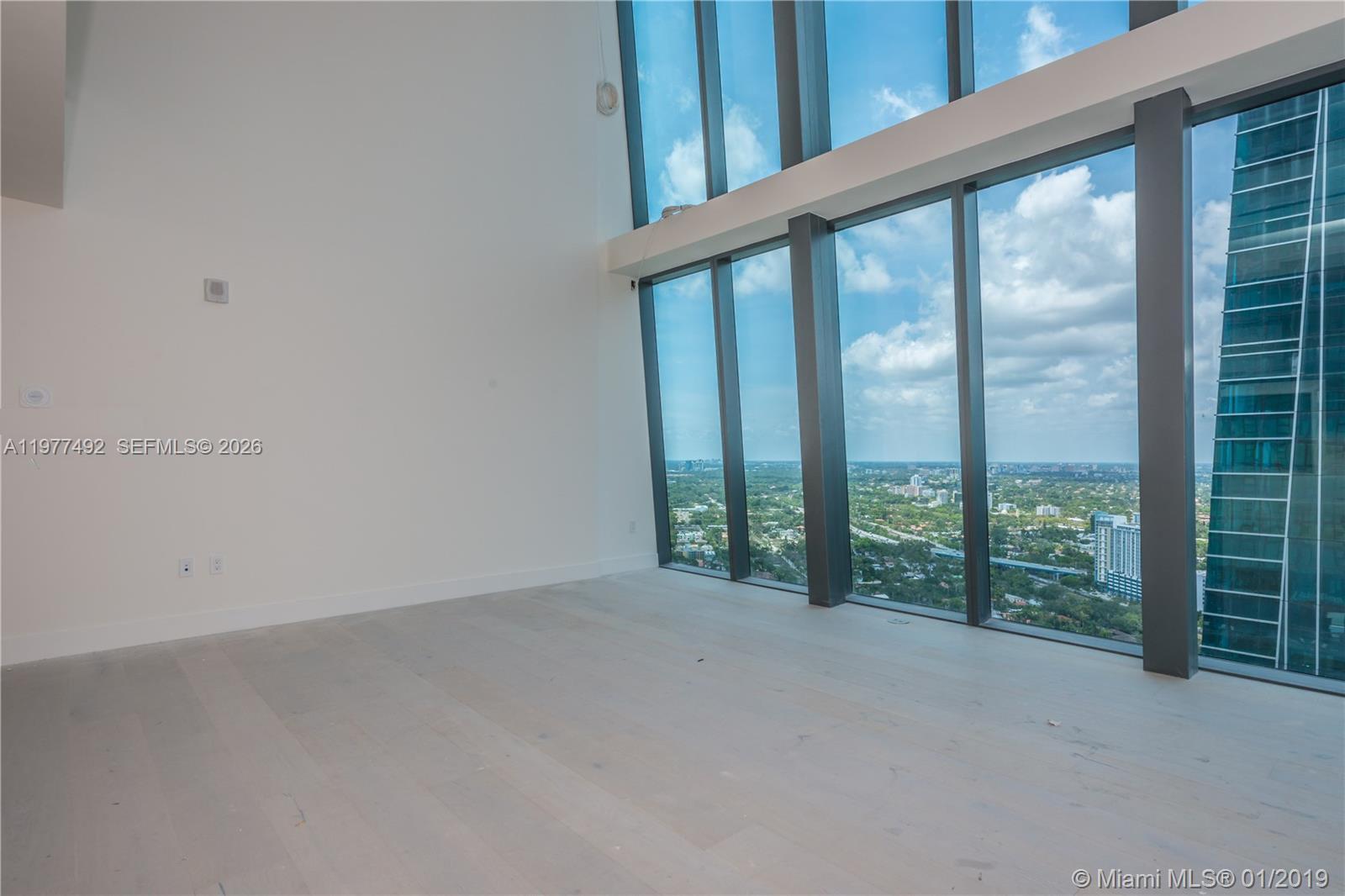 An empty room features light wood flooring and floor-to-ceiling windows with a city view — 1451 Brickell Ave # 4004, Miami FL 33131, MIAMI, FL