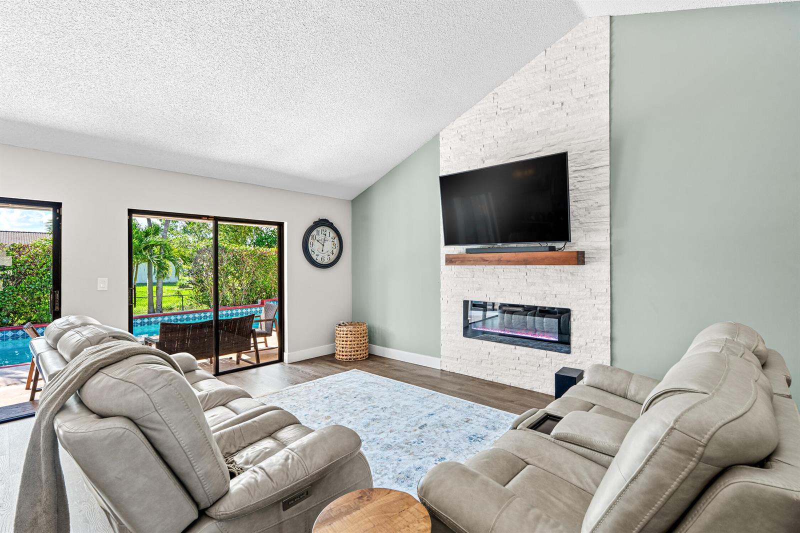 A living room features a white stone fireplace, a wall-mounted television, and a sliding glass door — 1912 NW 77th Avenue, Margate FL 33063, MARGATE, FL