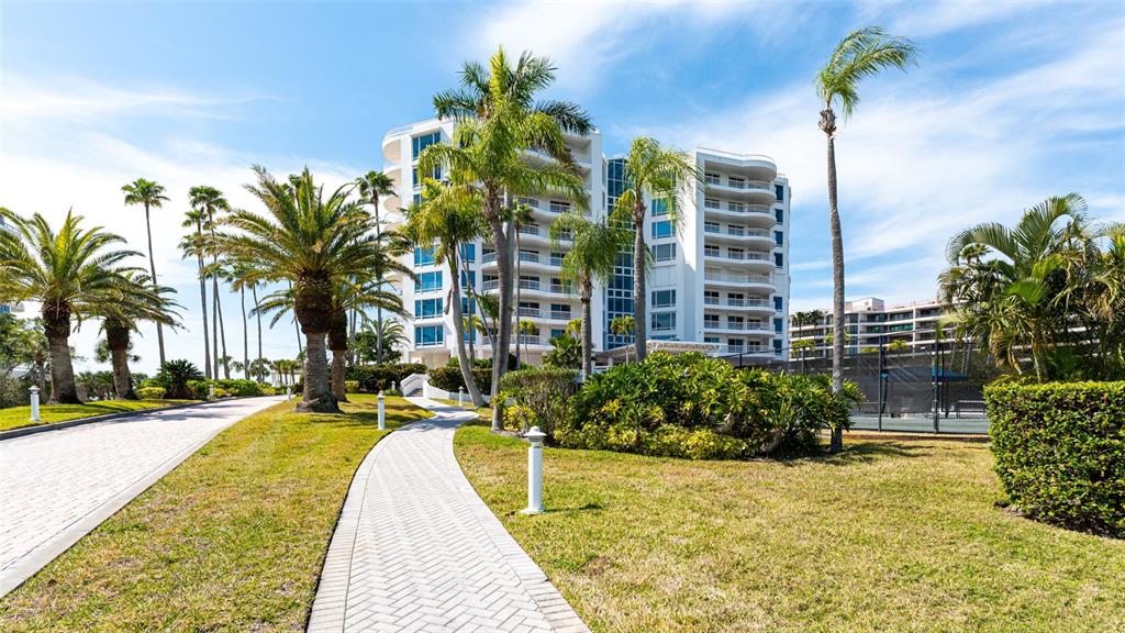 A paved walkway leads toward a multi-story white residential building surrounded by palm trees — 455 LONGBOAT CLUB ROAD UNIT PH1, LONGBOAT KEY, FL