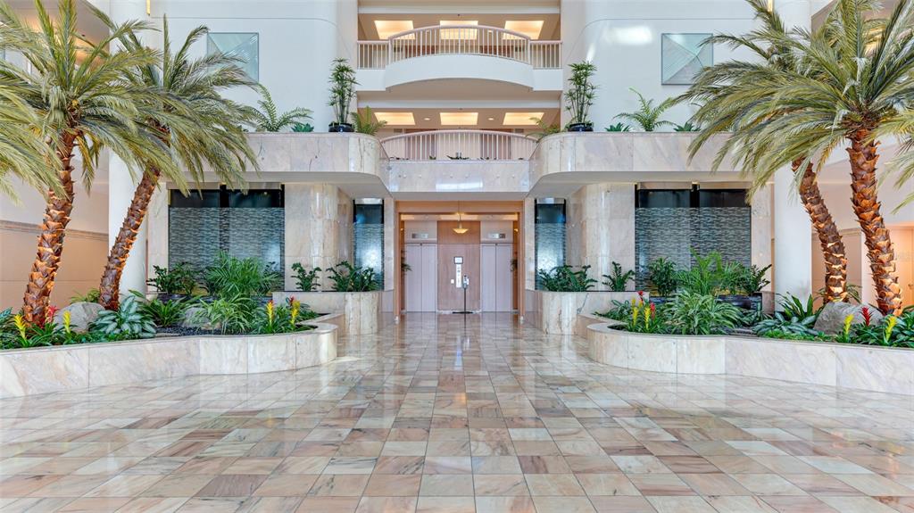 A grand lobby features marble floors, indoor palm trees, tiered planters, and a central elevator bank — 455 LONGBOAT CLUB ROAD UNIT PH1, LONGBOAT KEY, FL