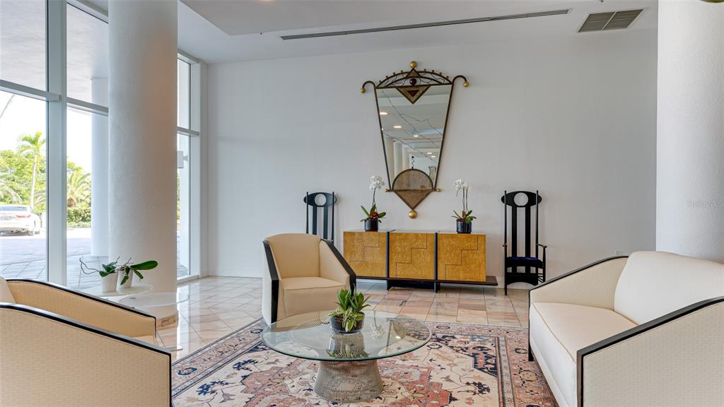 A bright lobby features a seating area with cream-colored furniture, a patterned rug, and a mirror — 455 LONGBOAT CLUB ROAD UNIT PH1, LONGBOAT KEY, FL