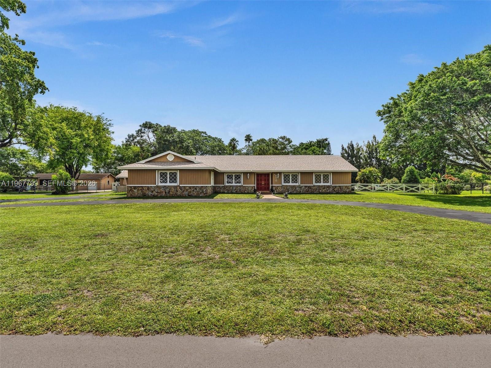 A single-story house with brown siding and a stone base sits behind a large lawn — 5310 SW 109th Ave, Davie FL 33328, DAVIE, FL