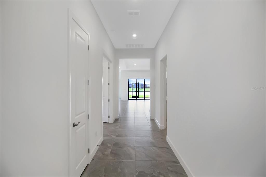 A hallway with white walls and gray tile flooring leads toward a glass-paned exterior door — 17212 LUMINOUS AVENUE, VENICE, FL
