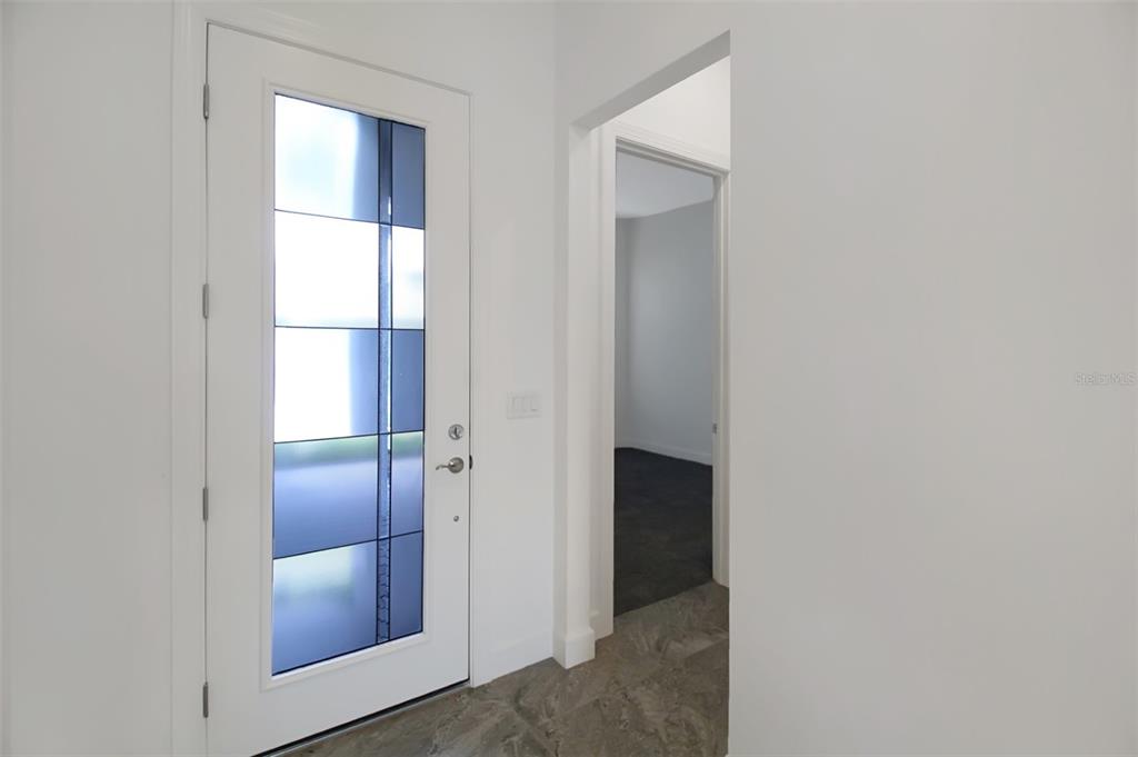 A white front door with a glass panel opens into a foyer with tiled flooring — 17212 LUMINOUS AVENUE, VENICE, FL