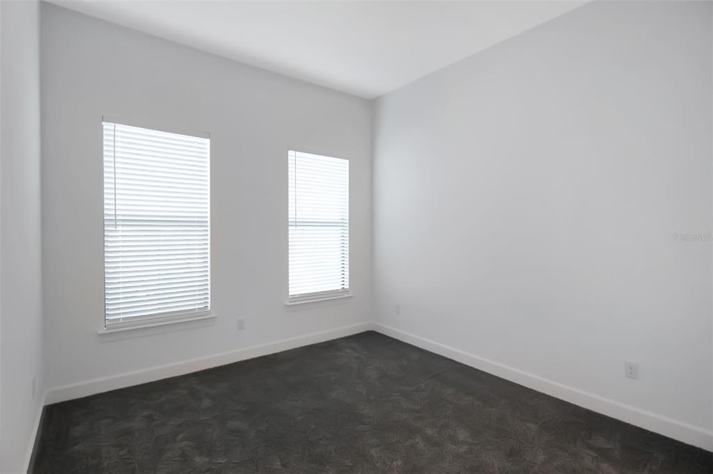 An empty bedroom features white walls, dark gray carpeting, and two windows with white blinds — 17212 LUMINOUS AVENUE, VENICE, FL