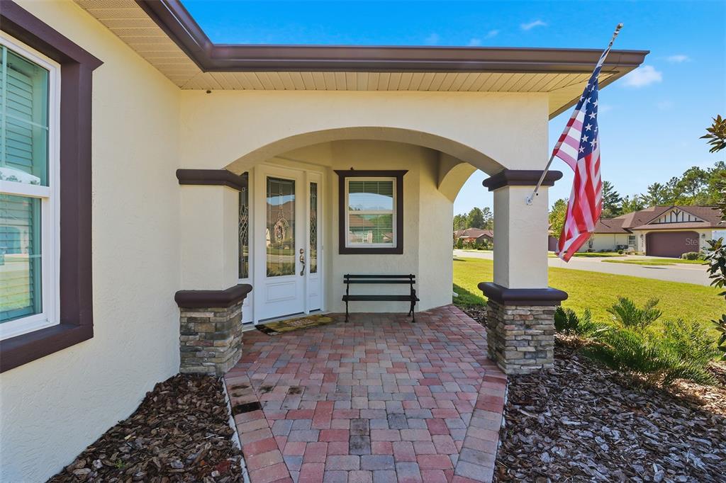 A covered front porch features brick pavers, stone-based columns, and an American flag — 5470 W HUNTER RUN LANE, HOMOSASSA, FL