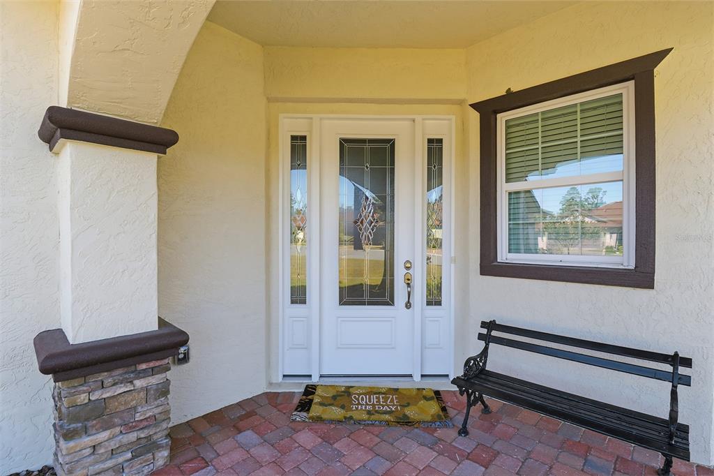 A front porch features a white door with glass panels, a brick floor, and a bench — 5470 W HUNTER RUN LANE, HOMOSASSA, FL