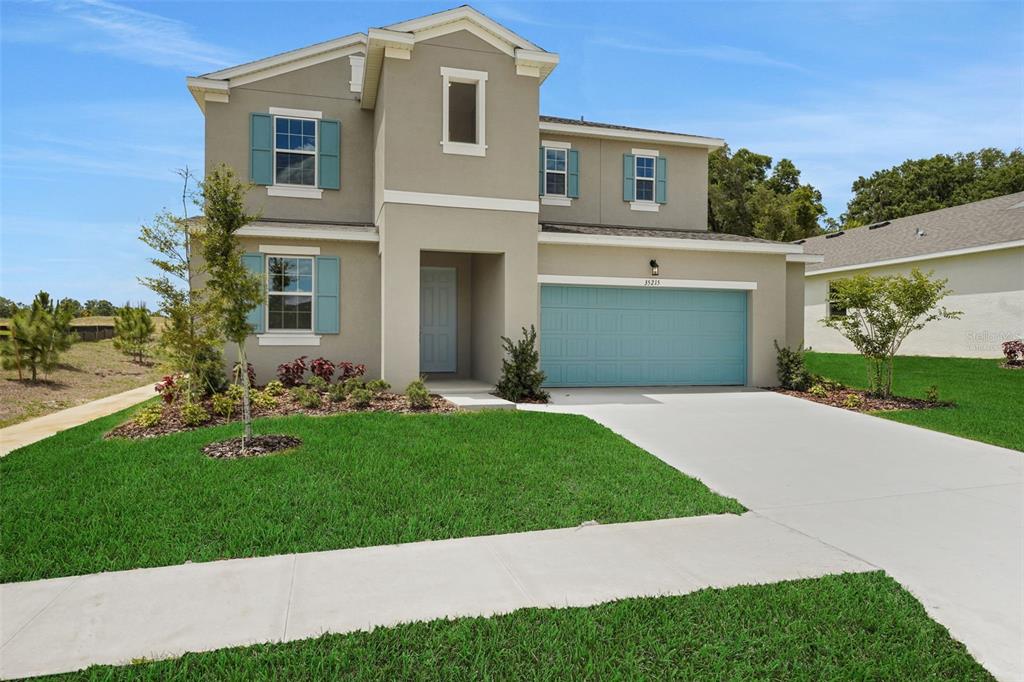 A two-story suburban house with a beige stucco exterior, blue shutters, and a two-car garage — 35215 TUSCAN HILL ROAD, DADE CITY, FL