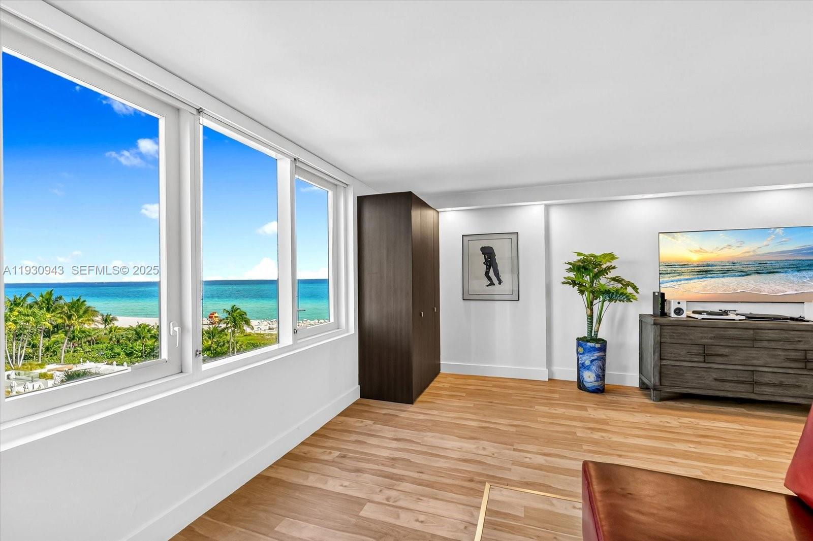 A living room features light wood flooring, a dark wardrobe, and large windows overlooking the ocean — 2301 Collins Ave # 714, Miami Beach FL 33139, MIAMI BEACH, FL