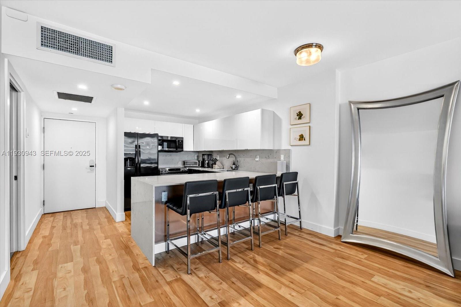A modern kitchen features white cabinetry, a stone-topped island with bar stools, and hardwood flooring — 2301 Collins Ave # 714, Miami Beach FL 33139, MIAMI BEACH, FL