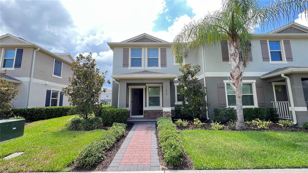 A two-story townhouse with a brick walkway, palm tree, and landscaped front yard — 11056 GREAT ROCK STREET, WINTER GARDEN, FL