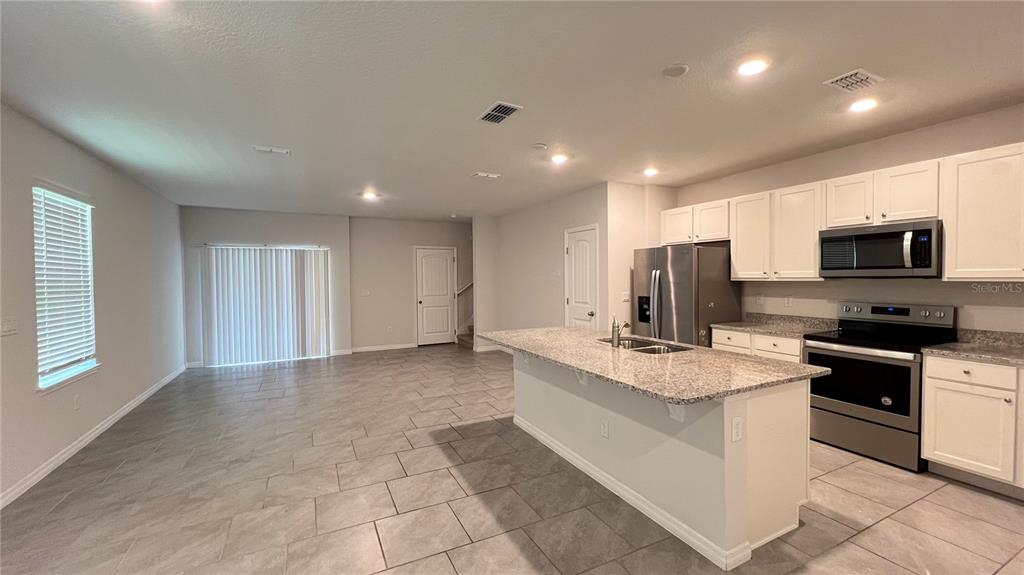 A kitchen with a granite island and white cabinets opens to a living area — 11056 GREAT ROCK STREET, WINTER GARDEN, FL