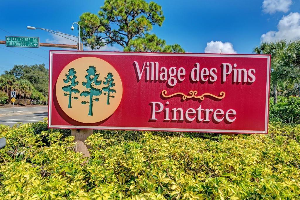 A red sign for Village des Pins Pinetree stands in front of green bushes and trees — 3645 WHITE PINE COURT UNIT 128, SARASOTA, FL