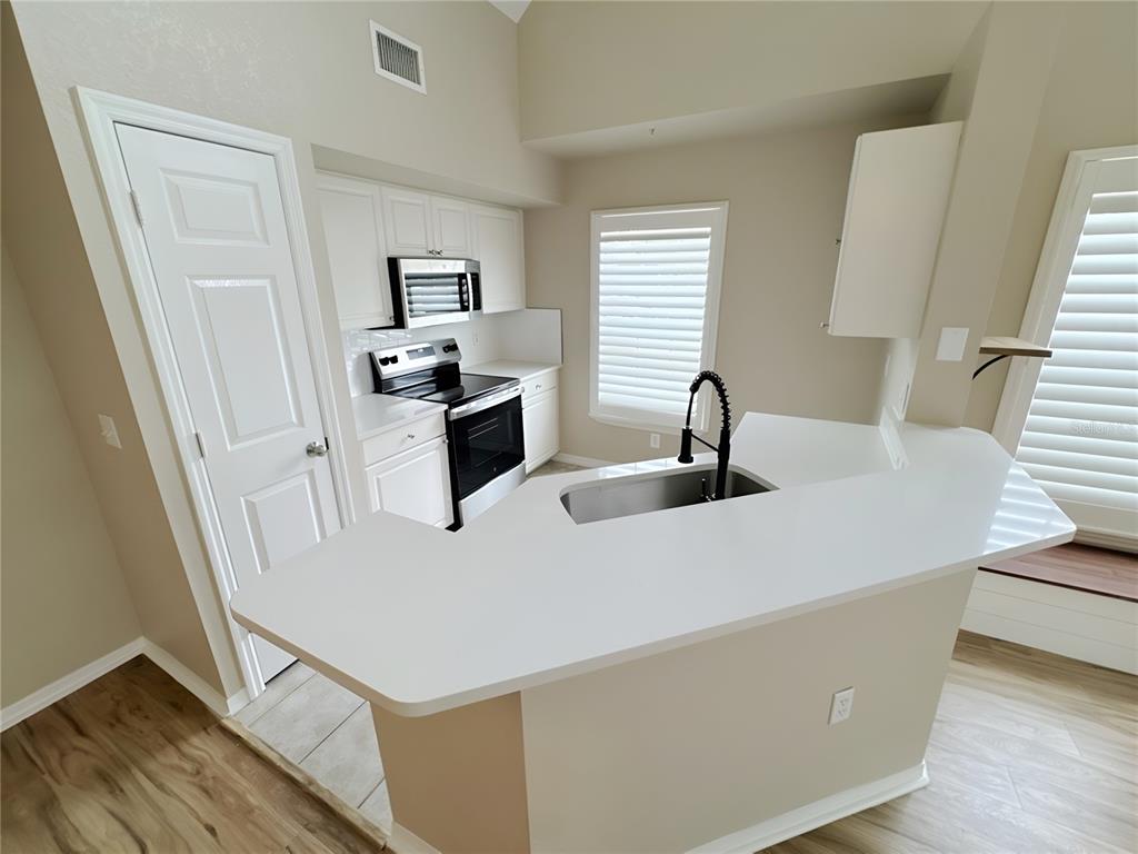 A kitchen features white cabinets, stainless steel appliances, and a white countertop breakfast bar — 5531 ROSEHILL ROAD UNIT 201, SARASOTA, FL