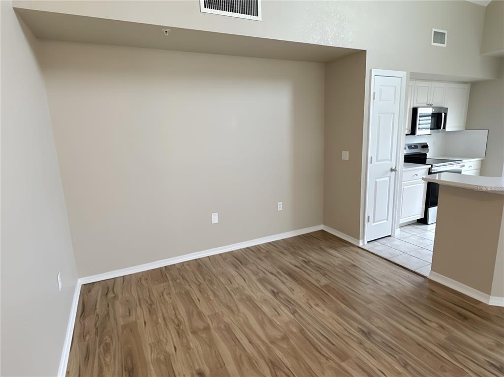 An empty room with light wood-look flooring and a recessed wall area near a kitchen — 5531 ROSEHILL ROAD UNIT 201, SARASOTA, FL