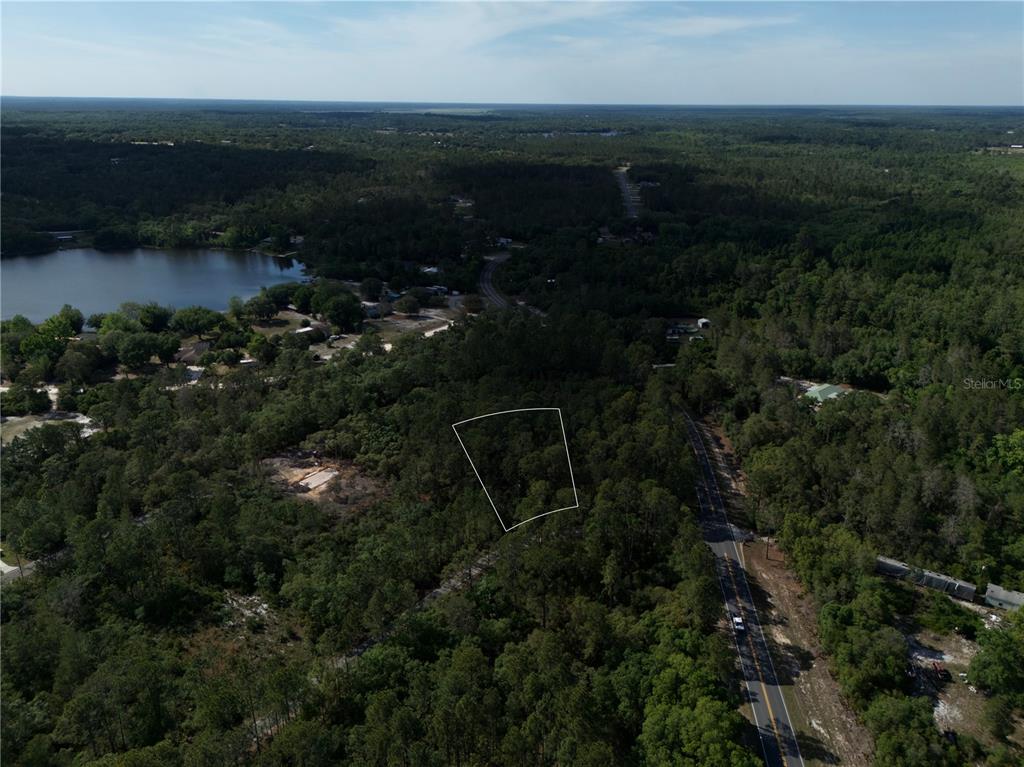 An aerial view shows a wooded lot outlined in white next to a paved road — 0 FISHER TRACE DR, OCKLAWAHA, FL