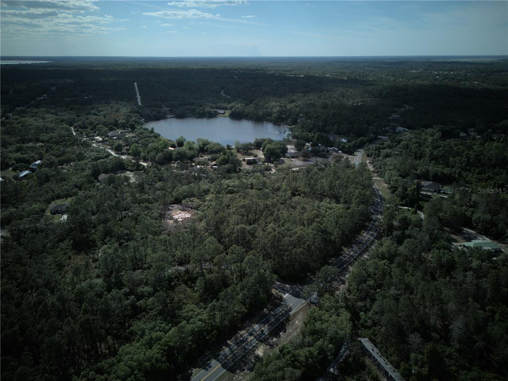 An aerial view shows a lake surrounded by dense forest and a winding road — 0 FISHER TRACE DR, OCKLAWAHA, FL