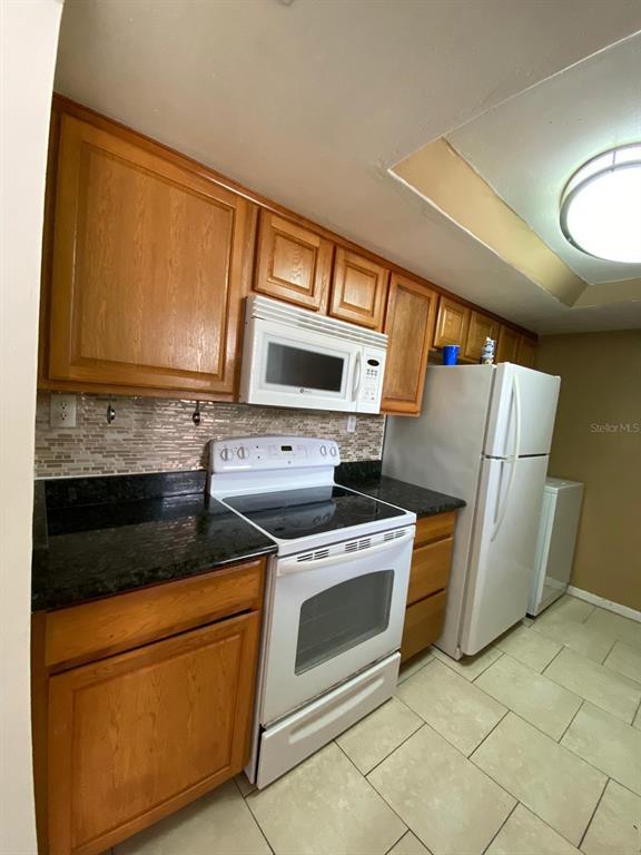 A galley kitchen features wood cabinets, dark countertops, white appliances, and light tile flooring — 2634 LEMON TREE LANE UNIT H, ORLANDO, FL