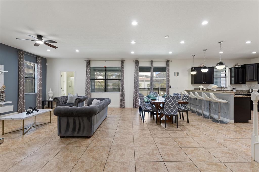 An open-concept living and dining area features tile flooring, a gray sofa, and kitchen bar seating — 1428 THUNDERBIRD ROAD, DAVENPORT, FL