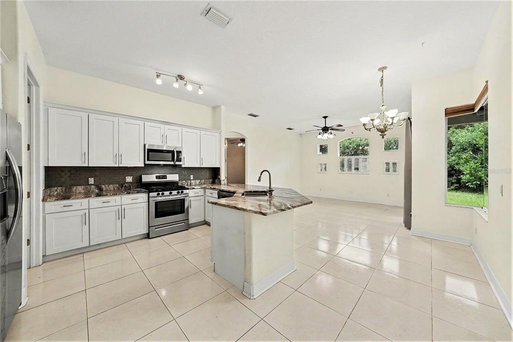 A kitchen with white cabinets, granite countertops, and tile flooring opens into a dining area — 12516 LEATHERLEAF DRIVE, TAMPA, FL