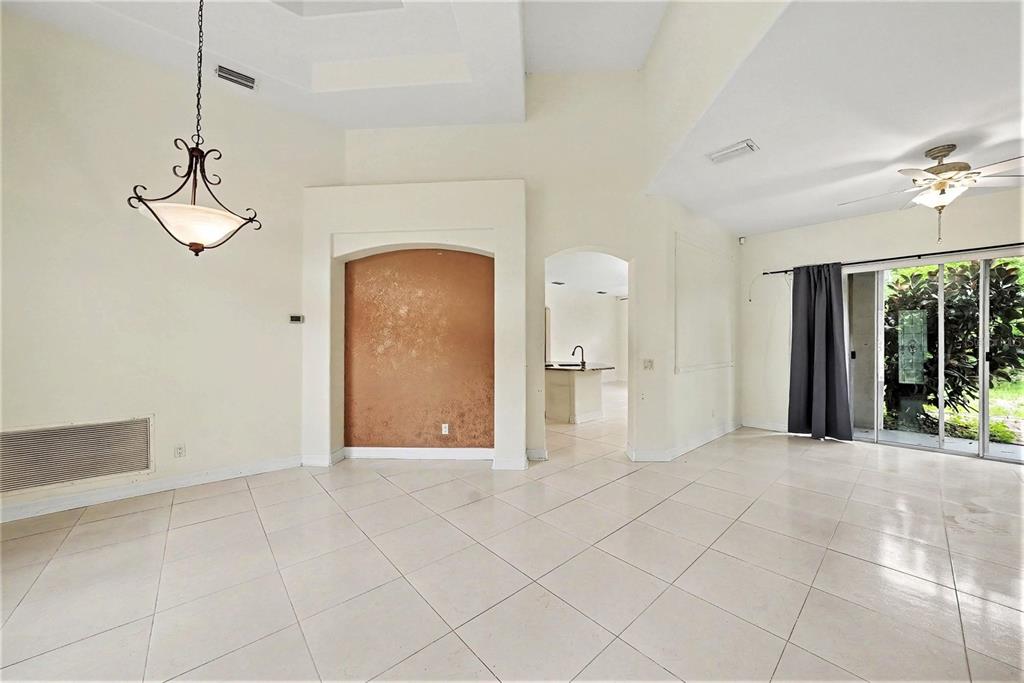 A bright, tiled living room features a decorative arched alcove and sliding glass patio doors — 12516 LEATHERLEAF DRIVE, TAMPA, FL