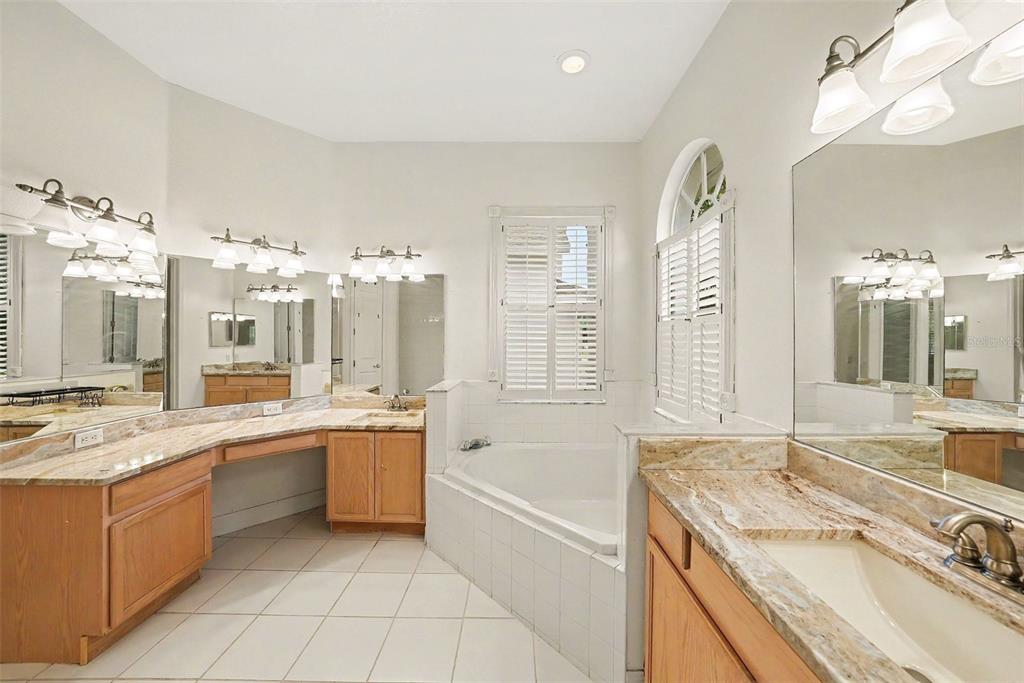 A bathroom features dual wooden vanities with granite countertops, a corner soaking tub, and tile flooring — 12516 LEATHERLEAF DRIVE, TAMPA, FL
