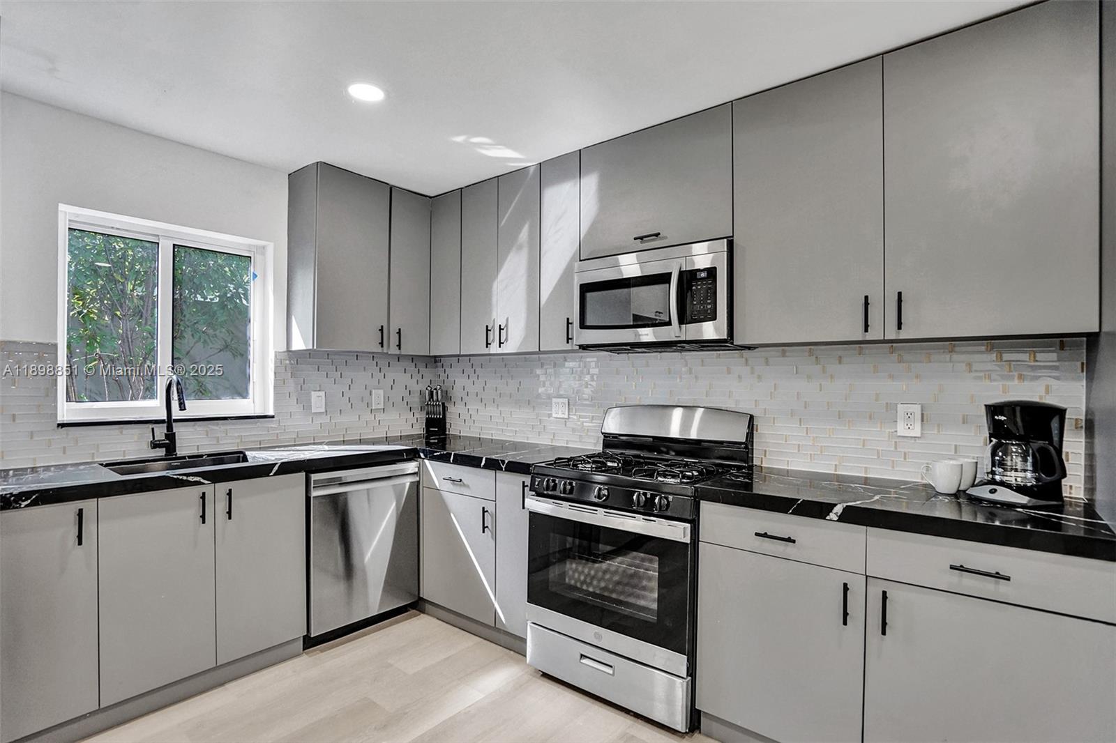 A kitchen features gray cabinets, black countertops, stainless steel appliances, and a light-colored tile backsplash — 1230 Johnson St, Hollywood FL 33019, HOLLYWOOD, FL