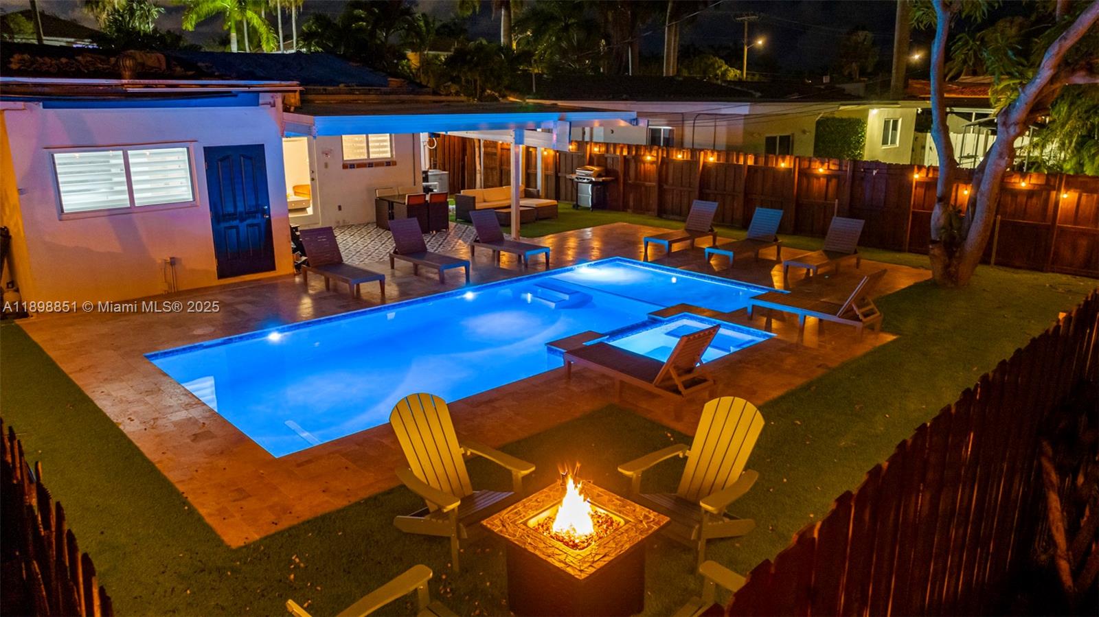 An illuminated backyard features a swimming pool, hot tub, fire pit, and lounge chairs — 1230 Johnson St, Hollywood FL 33019, HOLLYWOOD, FL