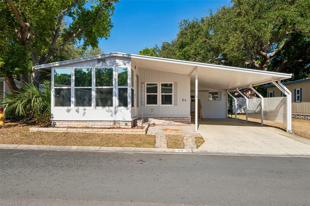 A single-story manufactured home with a carport and a large enclosed front porch — 7777 46TH AVENUE N UNIT 84, ST PETERSBURG, FL