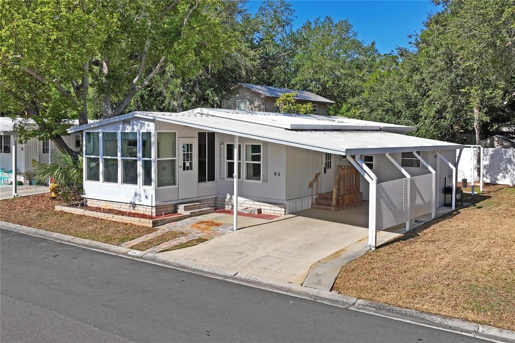 A single-story manufactured home features a white metal exterior, a carport, and a sunroom — 7777 46TH AVENUE N UNIT 84, ST PETERSBURG, FL