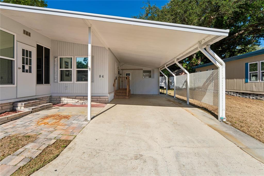 A mobile home exterior features a concrete driveway, a covered carport, and a paved patio — 7777 46TH AVENUE N UNIT 84, ST PETERSBURG, FL