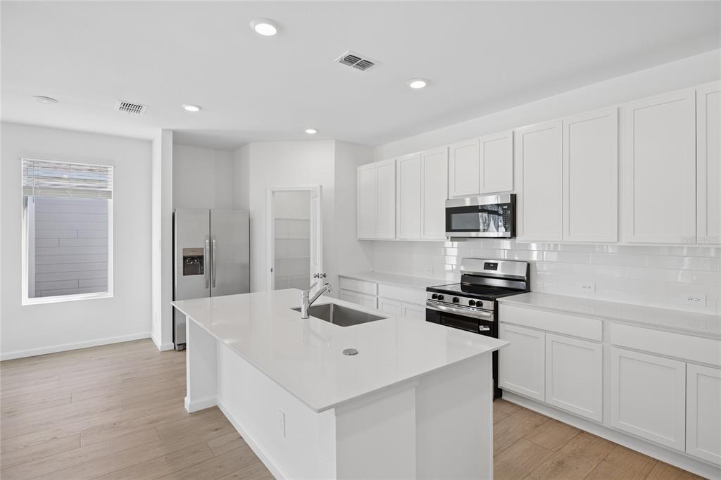 A modern kitchen features white cabinetry, a large quartz island, stainless steel appliances, and wood-look flooring — 5087 LOGGIA LANE, KISSIMMEE, FL