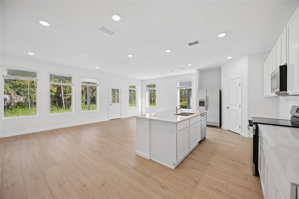 A bright, open-concept kitchen and living area featuring white cabinetry, an island, and wood flooring — 5087 LOGGIA LANE, KISSIMMEE, FL