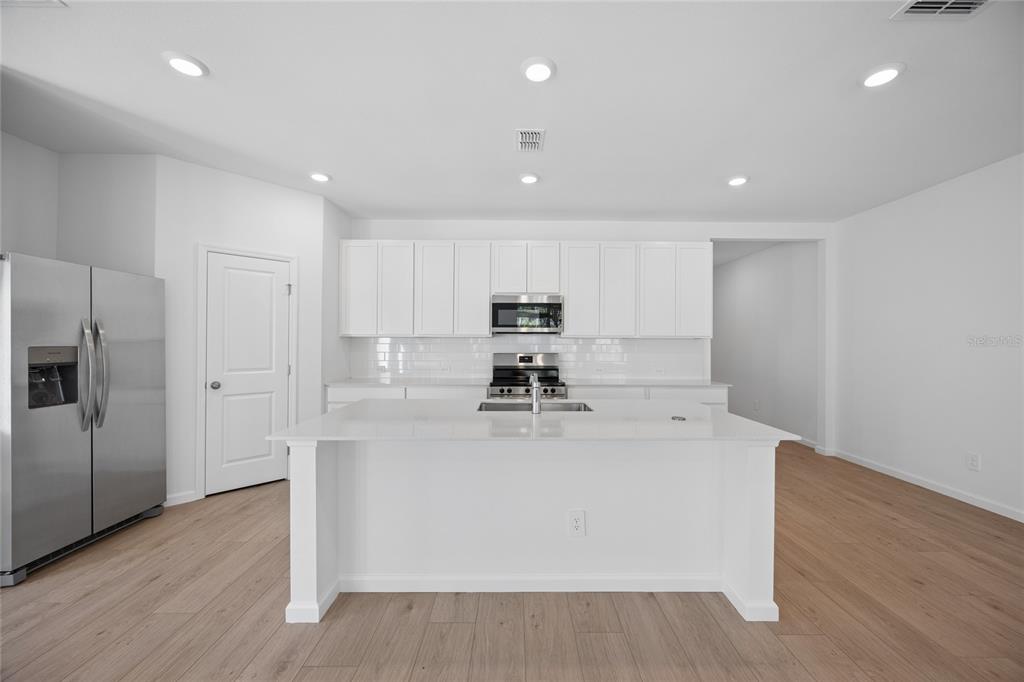 A modern kitchen features white cabinetry, stainless steel appliances, and a central island with seating — 5087 LOGGIA LANE, KISSIMMEE, FL