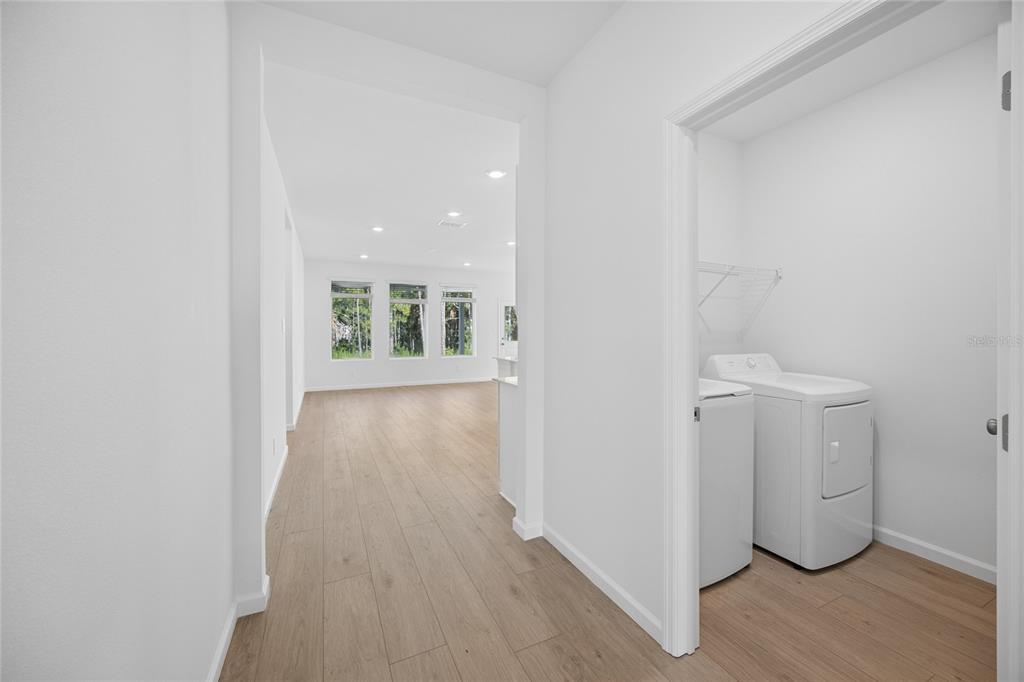 A hallway leads to a living area with light wood floors and a laundry closet — 5087 LOGGIA LANE, KISSIMMEE, FL