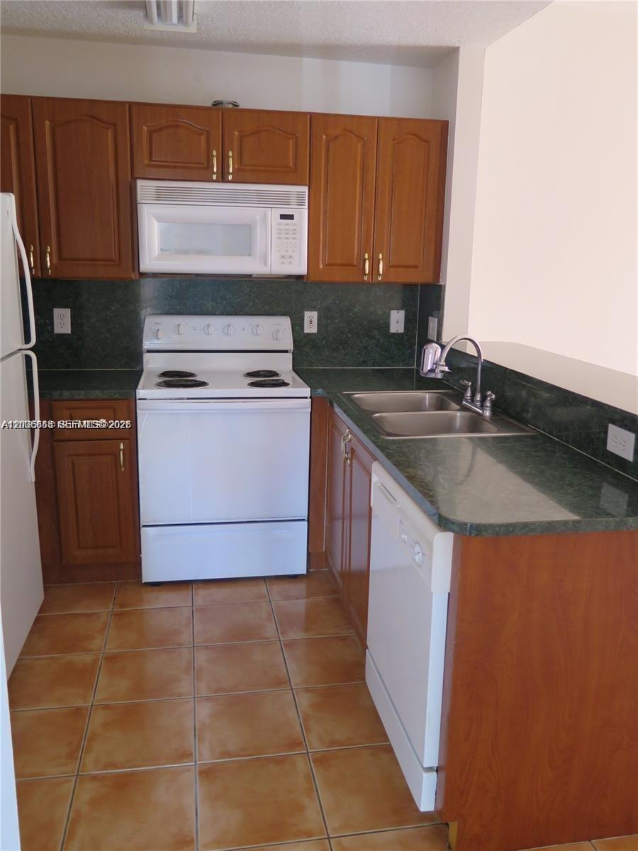 A kitchen features wood cabinets, green countertops, white appliances, and tiled flooring — 6202 NW 116th Pl # 443, Doral FL 33178, DORAL, FL