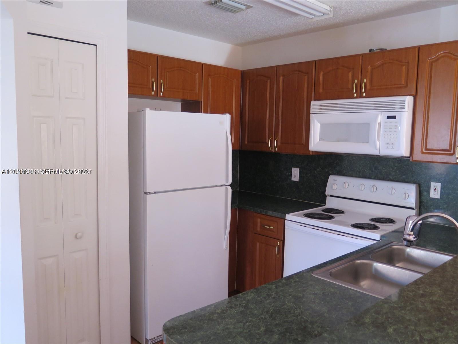 A kitchen features wood cabinets, white appliances, and a dark green laminate countertop — 6202 NW 116th Pl # 443, Doral FL 33178, DORAL, FL