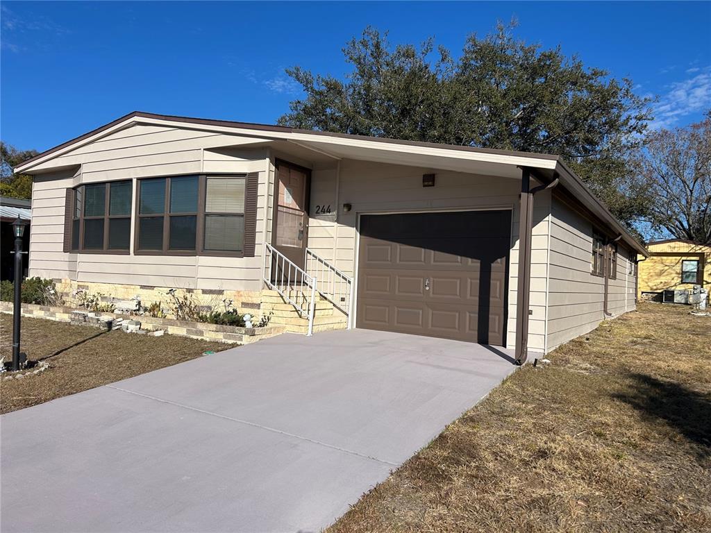 A single-story house with beige siding, a brown garage door, and a concrete driveway — 244 MENLO PARK AVENUE, DAVENPORT, FL