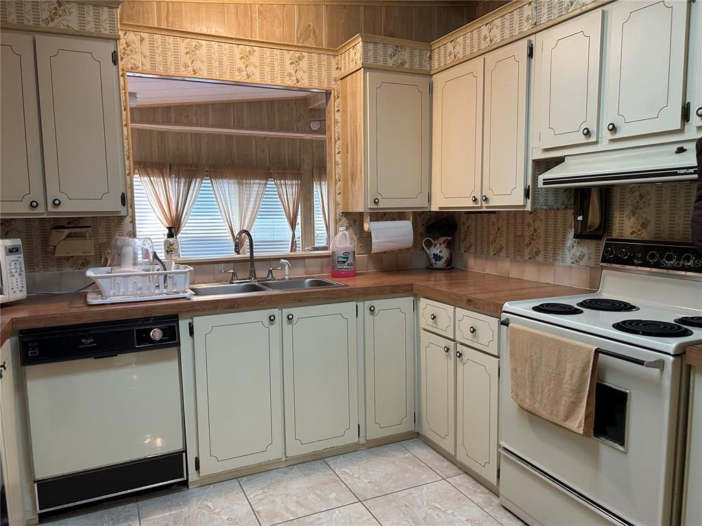 A kitchen features light-colored cabinets, a laminate countertop, a white stove, and floral wallpaper — 244 MENLO PARK AVENUE, DAVENPORT, FL