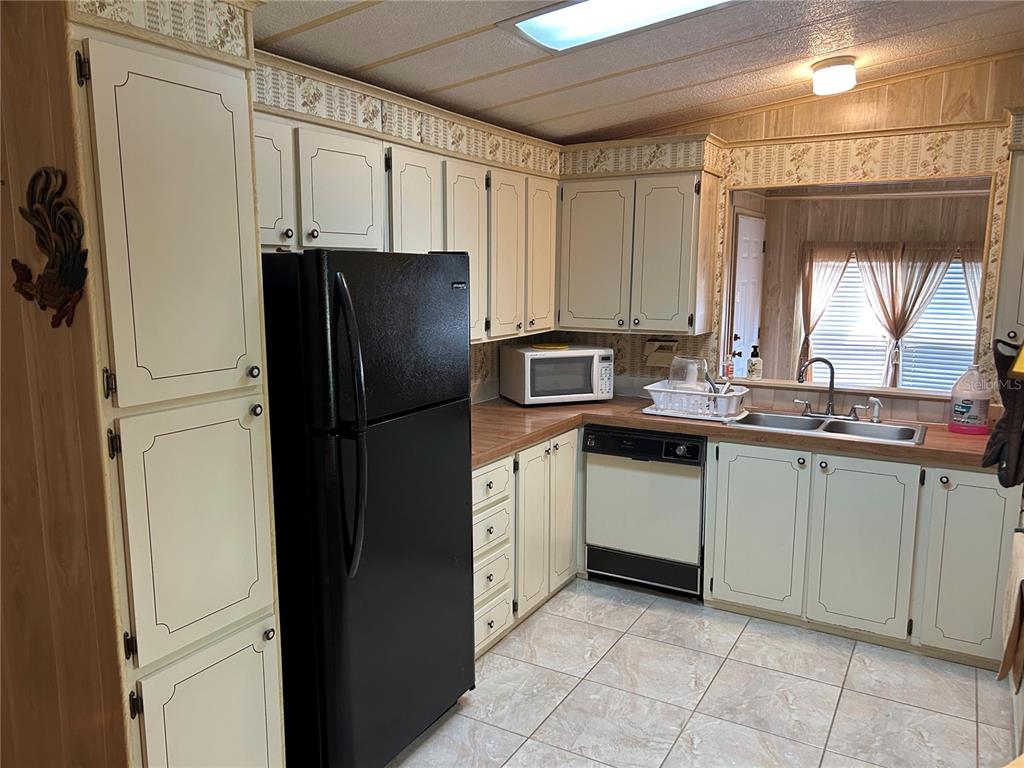 A kitchen features off-white cabinets, a black refrigerator, a dishwasher, and tile flooring — 244 MENLO PARK AVENUE, DAVENPORT, FL