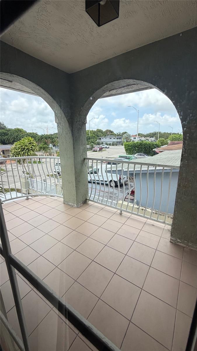 A tiled balcony features arched openings, white metal railings, and a view of a parking lot — 770 E 19th St # A, Hialeah FL 33013, HIALEAH, FL
